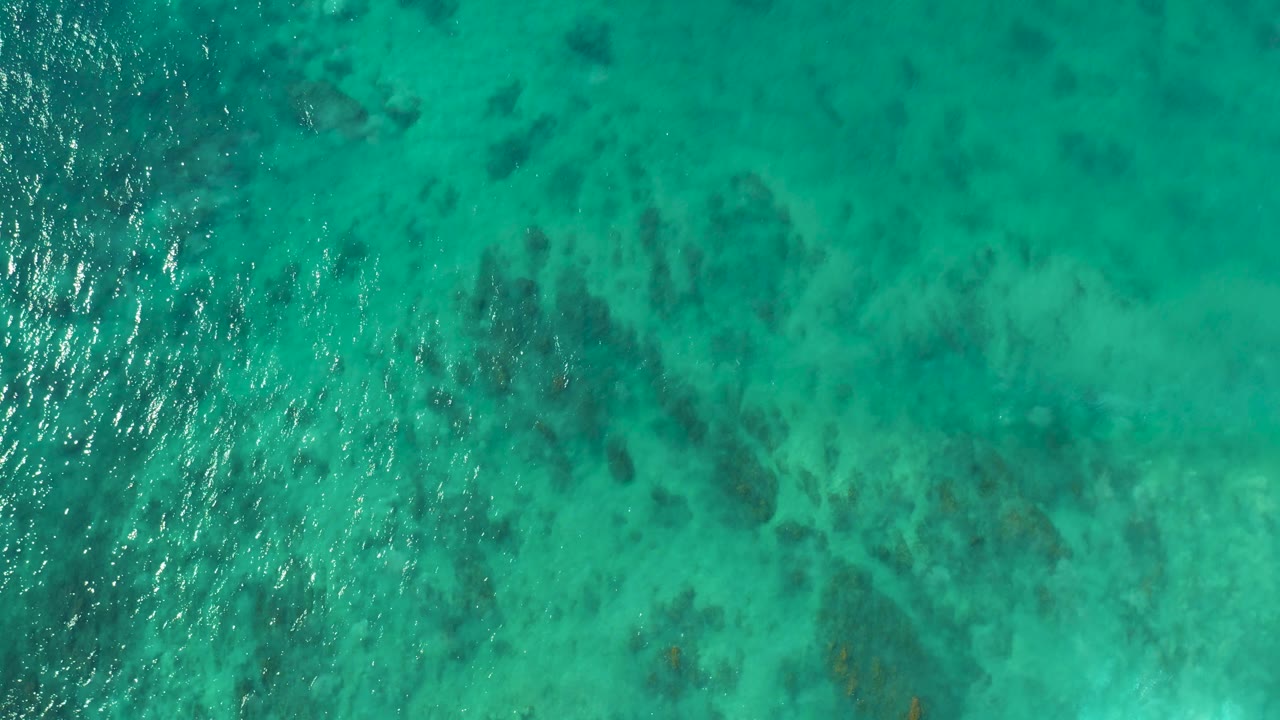 A second overhead frame shows turquoise water at San Luis Beach, East Cape, Los Cabos, Mexico, with a brighter vertical ripple band over darker submerged formations and no visible people.