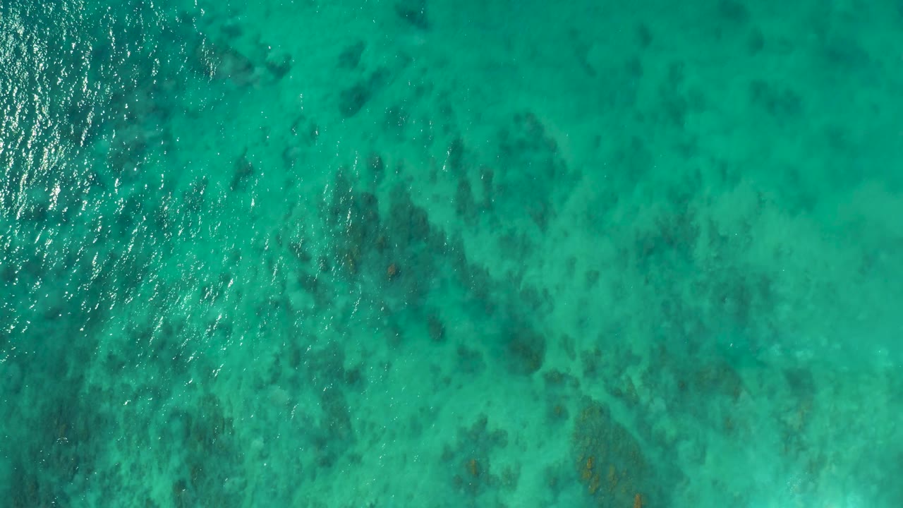 Aerial view of rippled turquoise water over darker seabed areas.