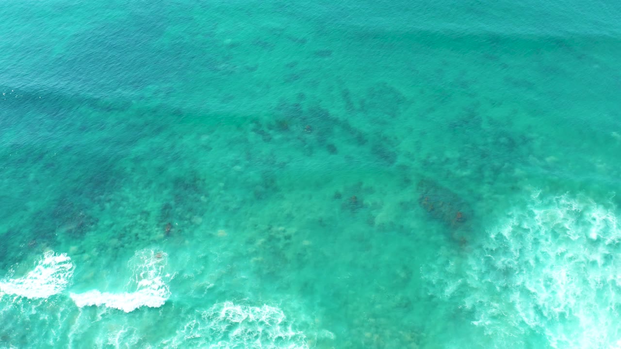 Turquoise ocean surface with reef shadows and breaking foam