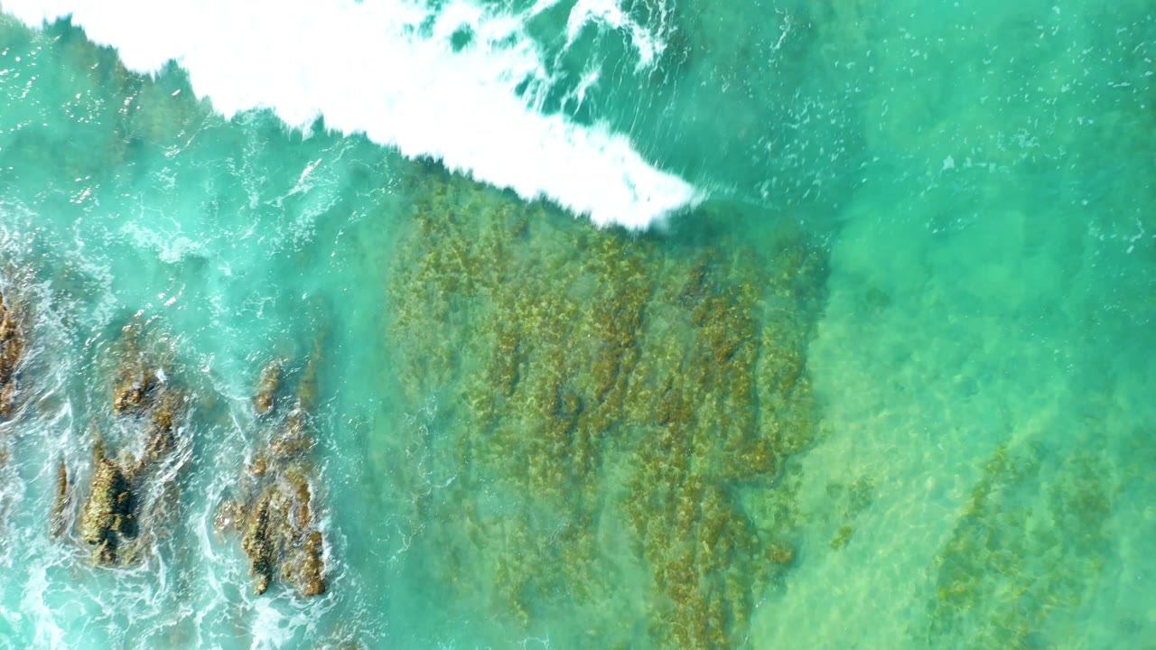 Overhead San Luis Beach East Cape Los Cabos Mexico view where a white wave edge pushes into turquoise water over dark rocks, with no visible people.