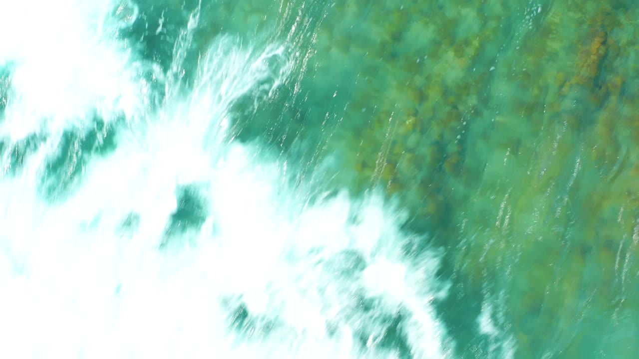 At San Luis Beach East Cape Los Cabos BCS Mexico, whitewater breaks across the upper frame and fades into turquoise water with patchy green-brown seabed detail, with no visible people.