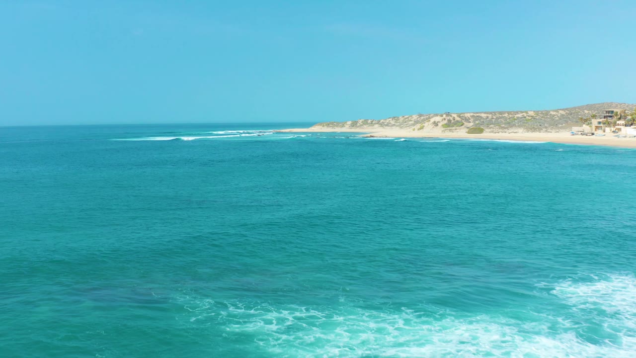 Blue-green water at San Luis Beach East Cape Los Cabos Mexico shows a wider white foam patch in the foreground and sandy beach in the distance, no visible people.
