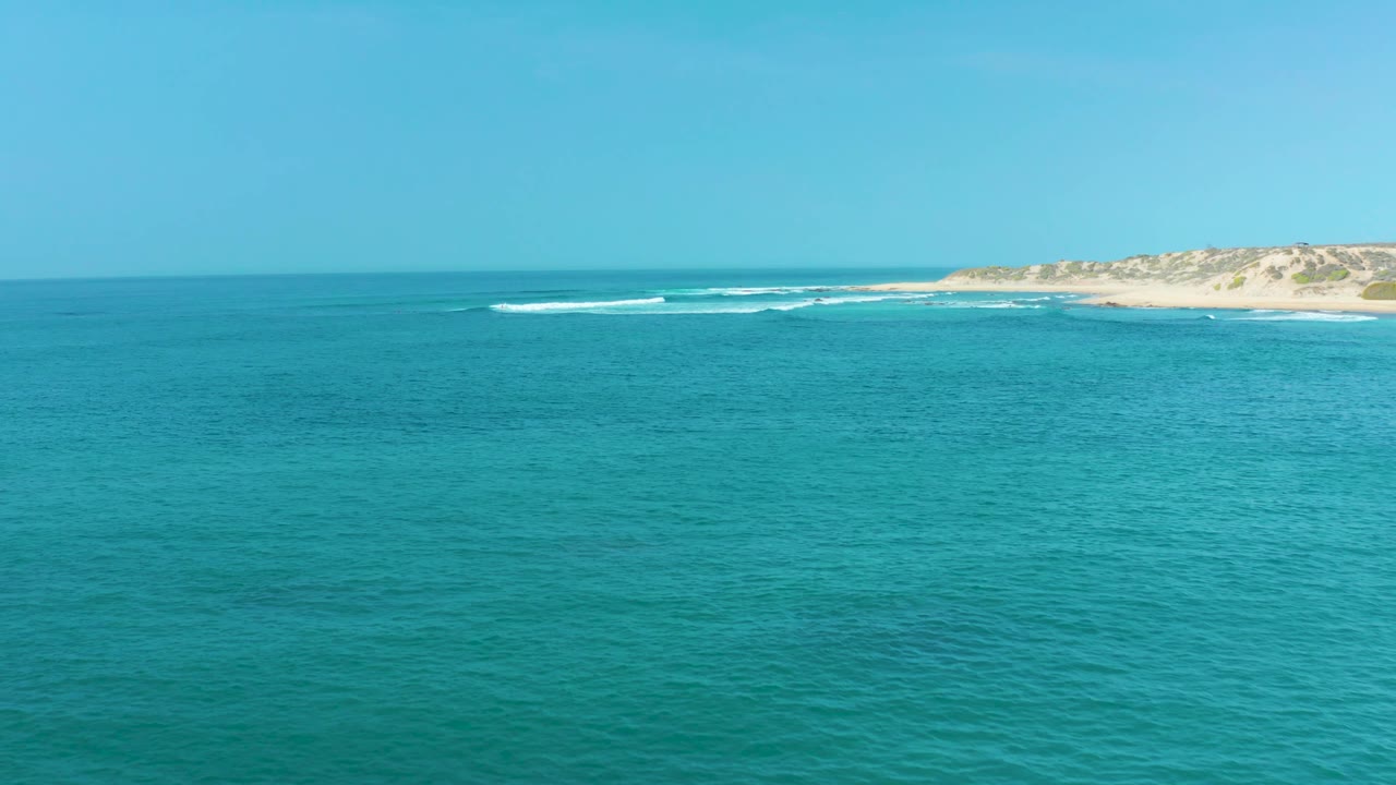 Open blue-green water facing a distant sandy shoreline
