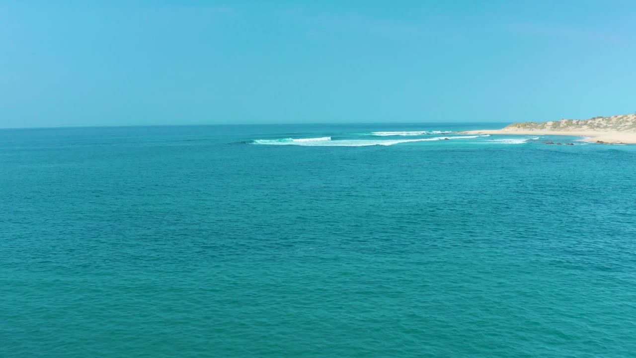 Turquoise sea with a low sandy coastline and gentle whitecaps in the distance.