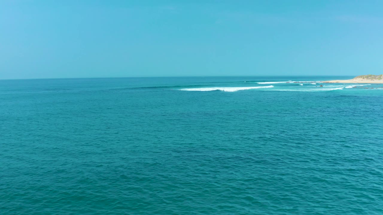 At San Luis Beach in Mexico, calm turquoise water leads toward distant white surf and a small sandy headland on the right, with no visible people.