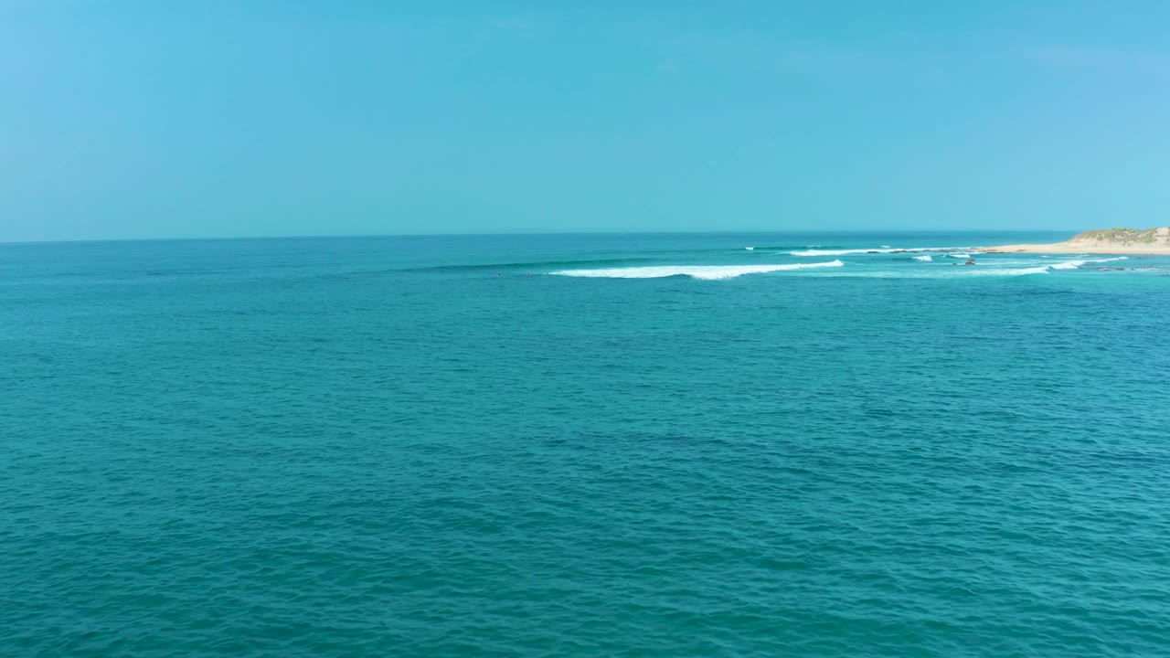 At San Luis Beach in Mexico, a wide field of turquoise ocean sits below the horizon while white wave breaks gather near the far coast, with no visible people.