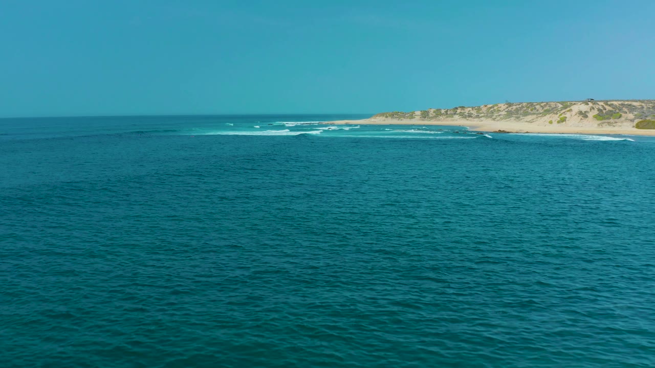 Ocean foreground with whitecaps along a sandy beach and dunes.