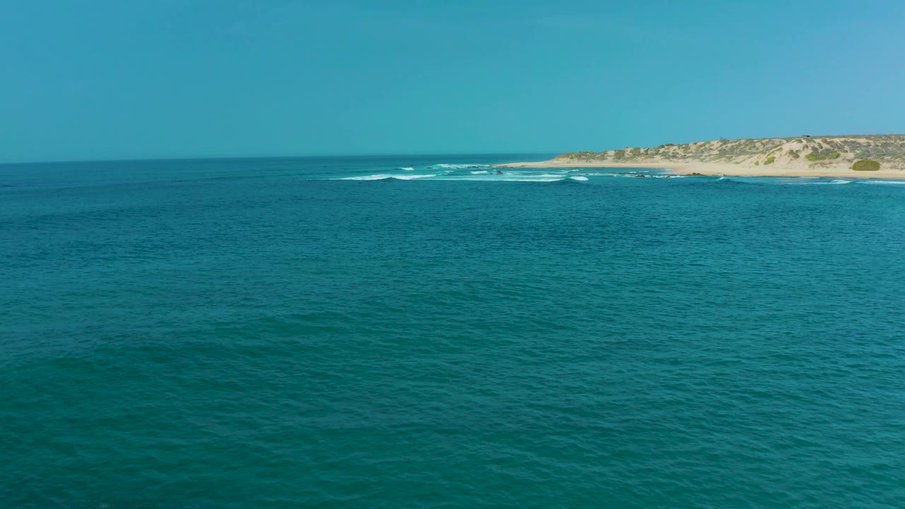 Turquoise ocean with distant sandy dunes and small surf lines