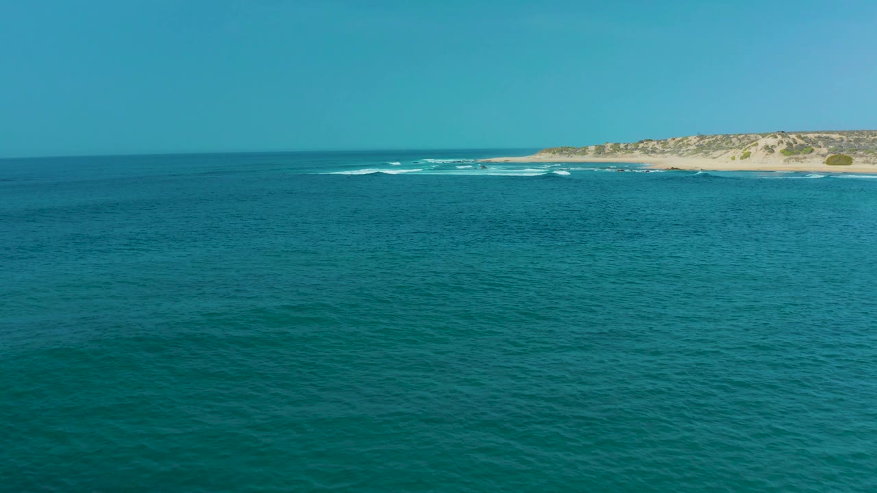Turquoise ocean fills most of the frame at San Luis Beach East Cape Los Cabos, with the sandy coast sitting farther right and no visible people.