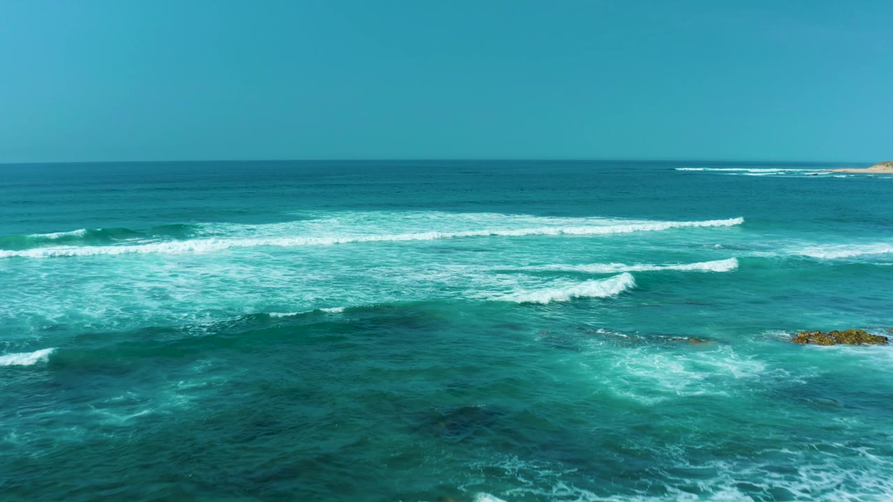 Blue-green ocean at San Luis Beach, East Cape Los Cabos, with several white wave lines, darker reef-like patches under the water, and no visible people.