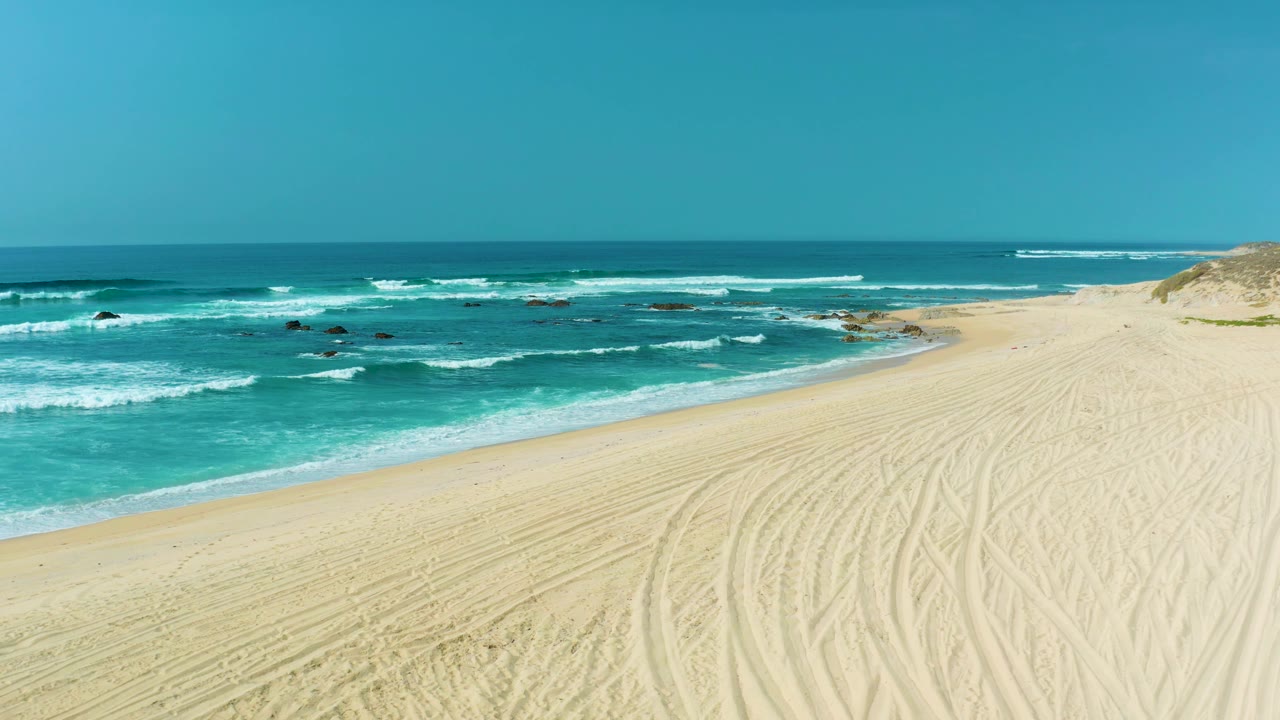 Foamy waves approach a broad sandy shoreline