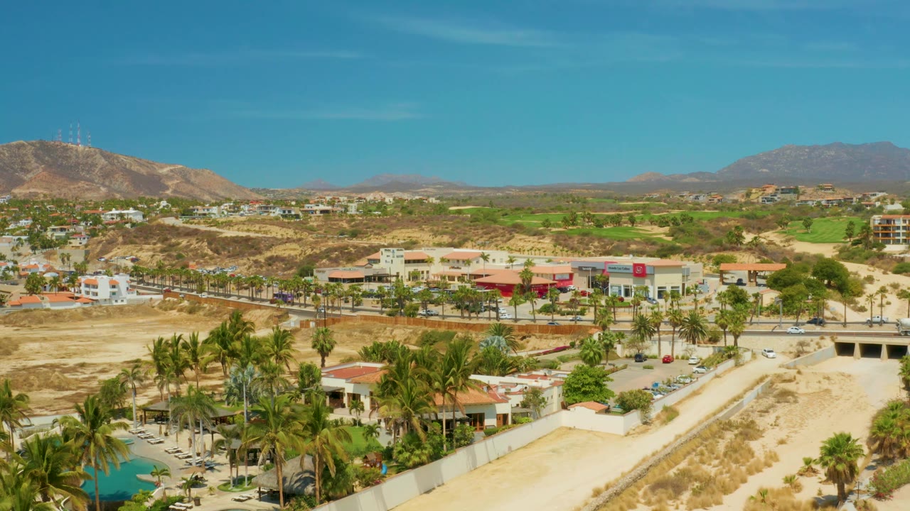 Wide elevated view of desert suburb, palm-lined road, and mountain ridge.