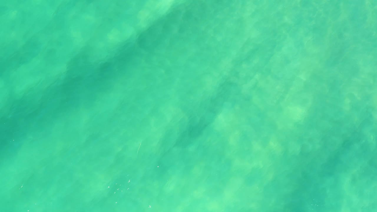 Shallow ocean surface with ripples over a pale sandy bottom.