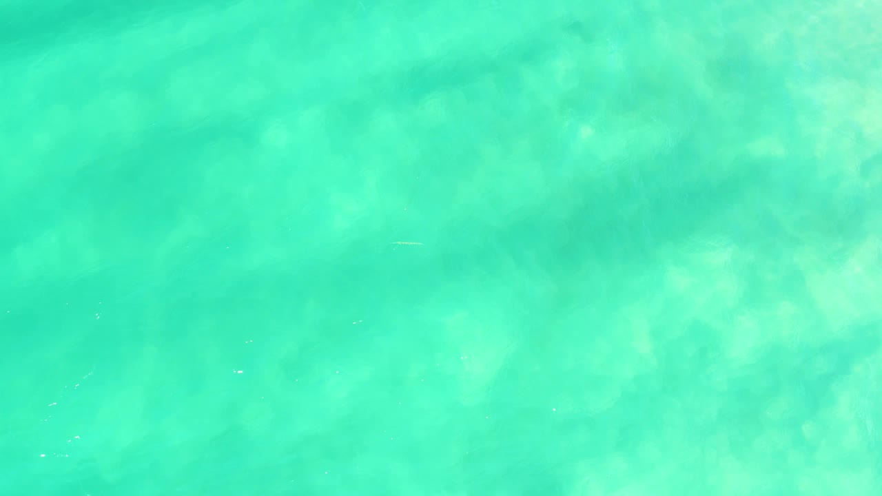 Turquoise shallow ocean water with sandy bottom texture.
