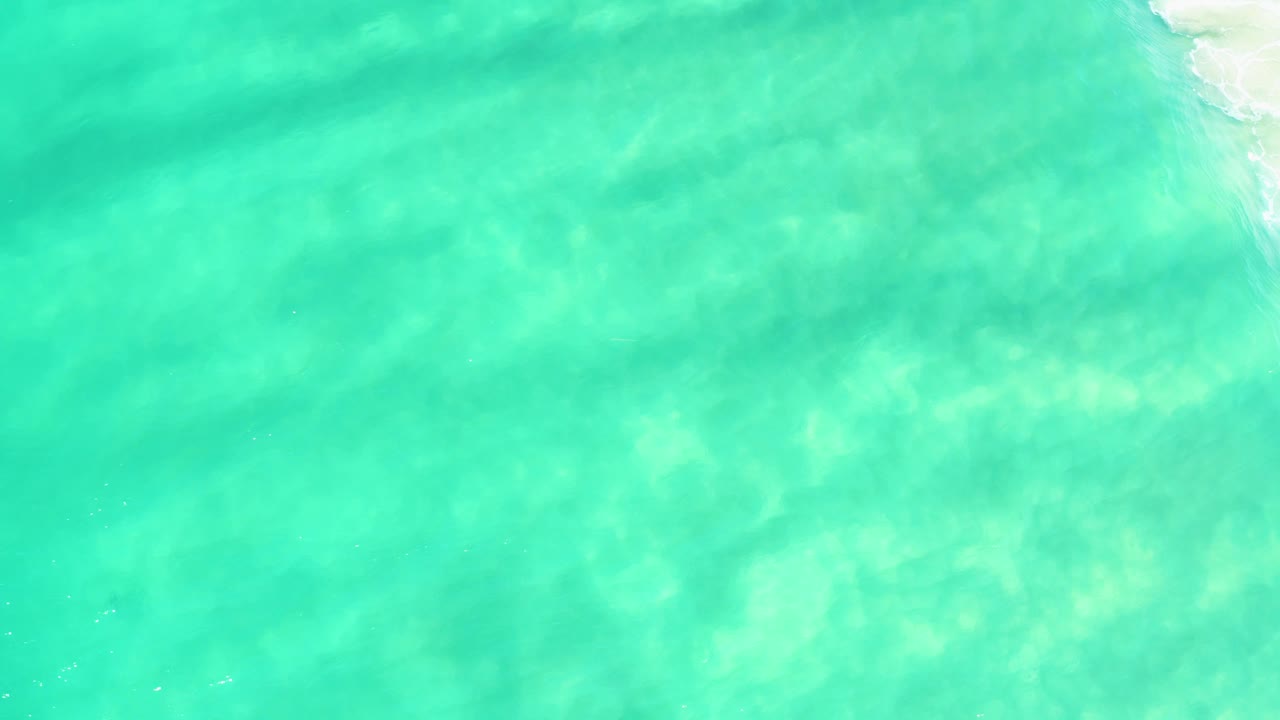 Transparent blue-green water over a sandy bottom in Campestre San Jose Del Cabo BCS Mexico, with the upper-right foam patch smaller than at the start and no visible people.