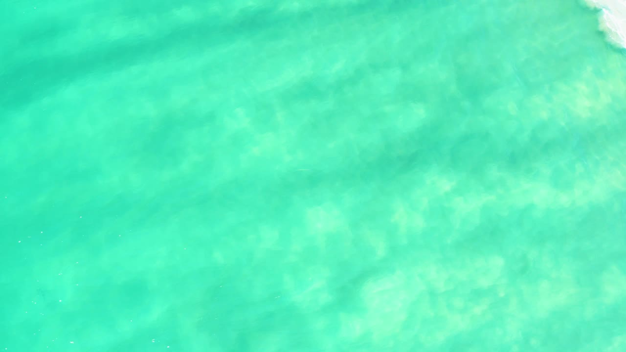 Mostly uninterrupted turquoise water in Campestre San Jose Del Cabo BCS Mexico, with mottled sandy texture under the surface and only a slight bright foam trace near the top edge, no visible people.