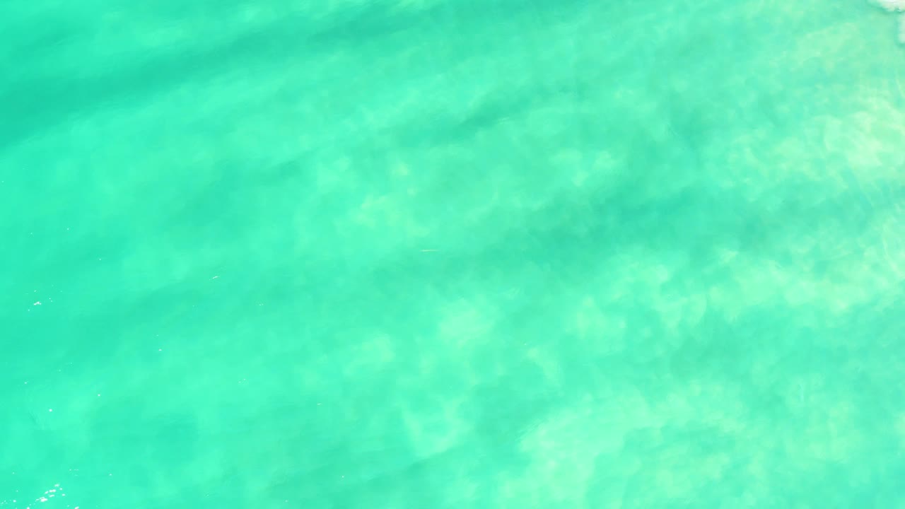 Overhead turquoise water in Campestre San Jose Del Cabo BCS Mexico, with darker diagonal underwater bands crossing the sandy bottom and no visible people.