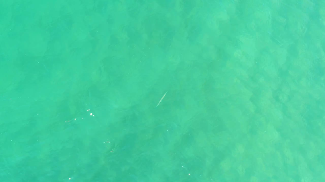 Turquoise shallow water with faint seabed texture and small surface reflections.