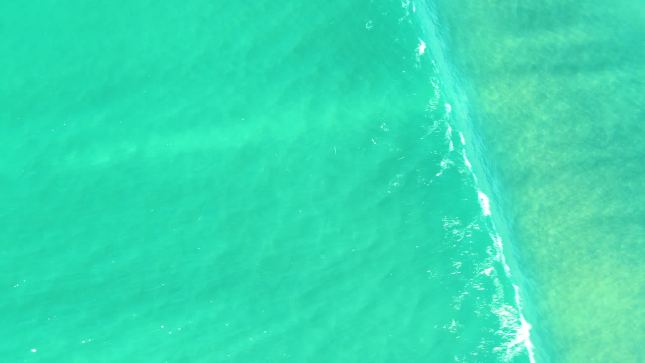 Top-down aerial view of turquoise ocean water in Campestre San Jose Del Cabo BCS Mexico, with a thin diagonal white foam line and no visible people.