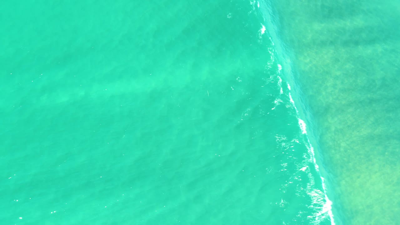 Aerial frame of clear turquoise water in Campestre San Jose Del Cabo BCS Mexico, with foam thinning near the center and no visible people.