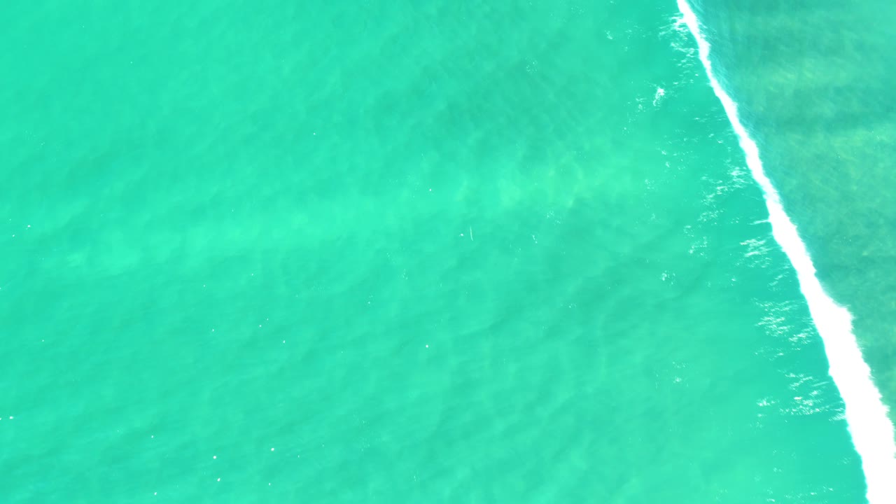 Top-down view of turquoise sea in Campestre San Jose Del Cabo BCS Mexico, with a bright white foam strip near the right edge and no visible people.
