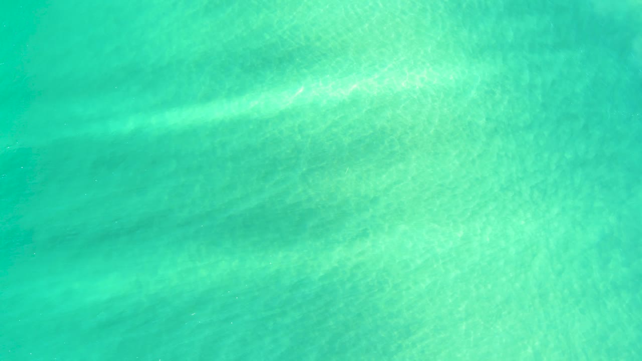 Overhead turquoise water detail in Campestre San Jose Del Cabo BCS Mexico, with pale sand showing through and diffuse ripple patterns, with no visible people.