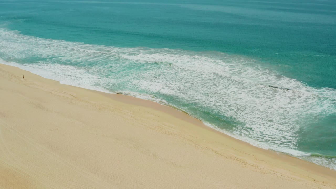 Aerial beach view in Campestre San Jose Del Cabo BCS Mexico, with a broad band of white surf pushing farther across the turquoise water and pale sand below.