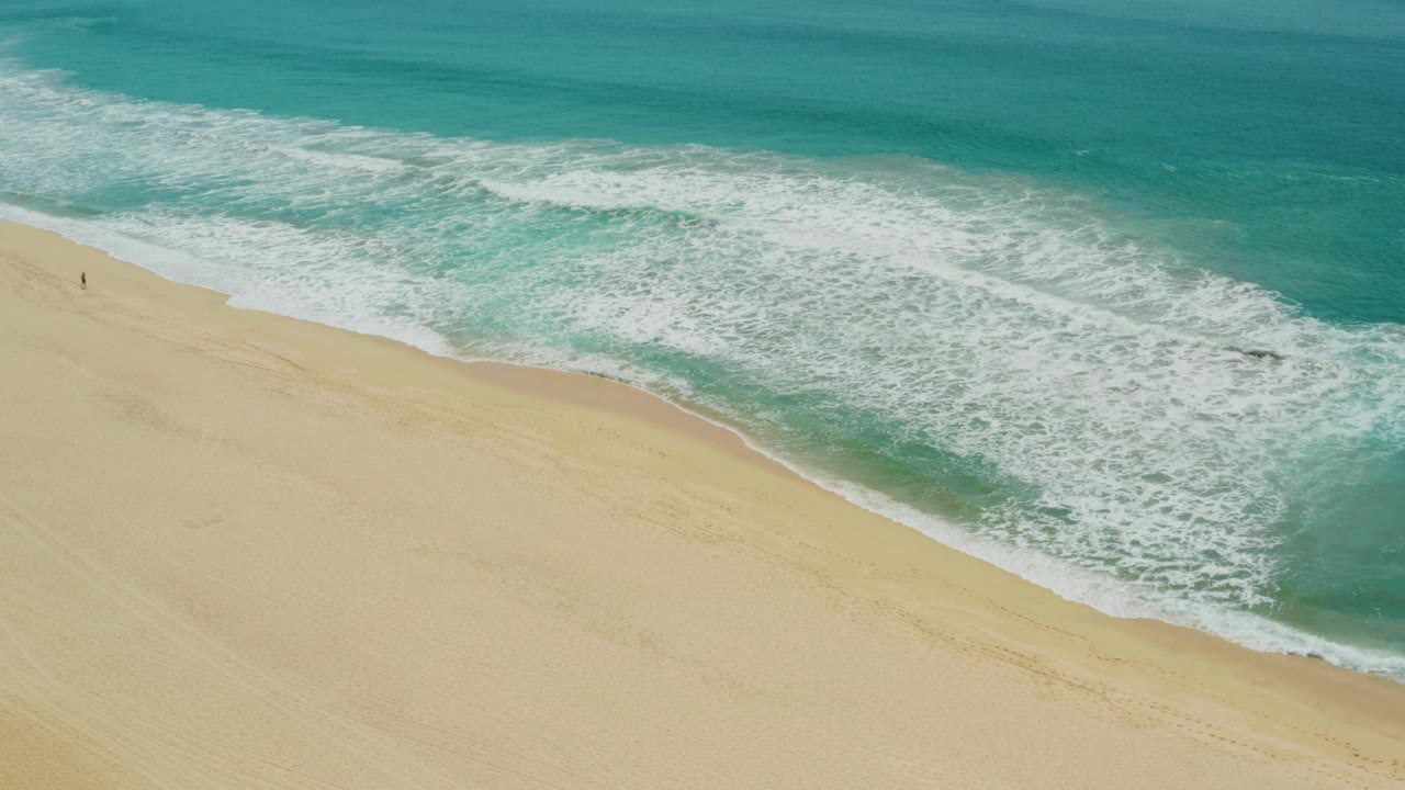 Aerial frame over Campestre San Jose Del Cabo BCS Mexico where the foamy wave edge curls across the upper beach and the sand remains mostly empty below.