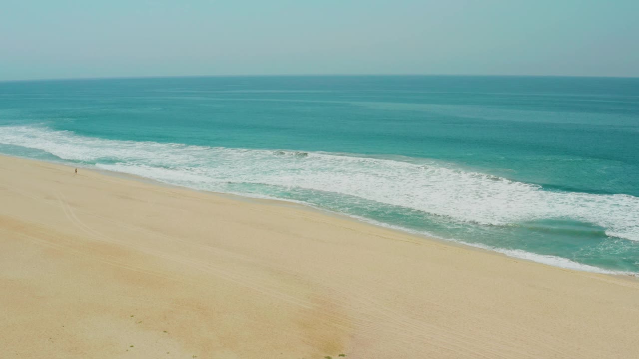 Campestre San Jose Del Cabo BCS Mexico beach frame with open sand filling the foreground, a broad white wave line crossing the shore, turquoise sea beyond, and no discernible people.