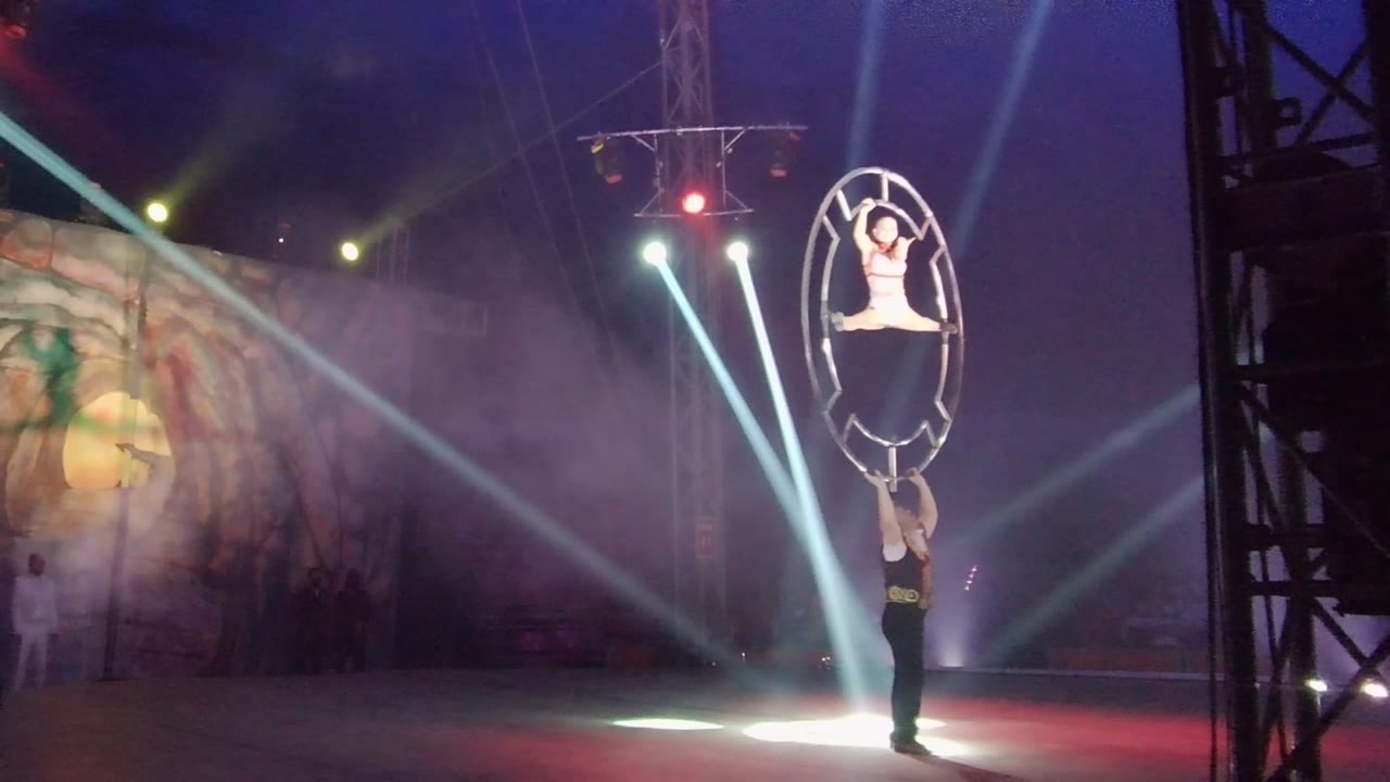 At 0:02 in San Jose del Cabo BCS Mexico, the hoop act appears farther right in frame beside a dark vertical truss, with blue haze, white beams, and a red light overhead.