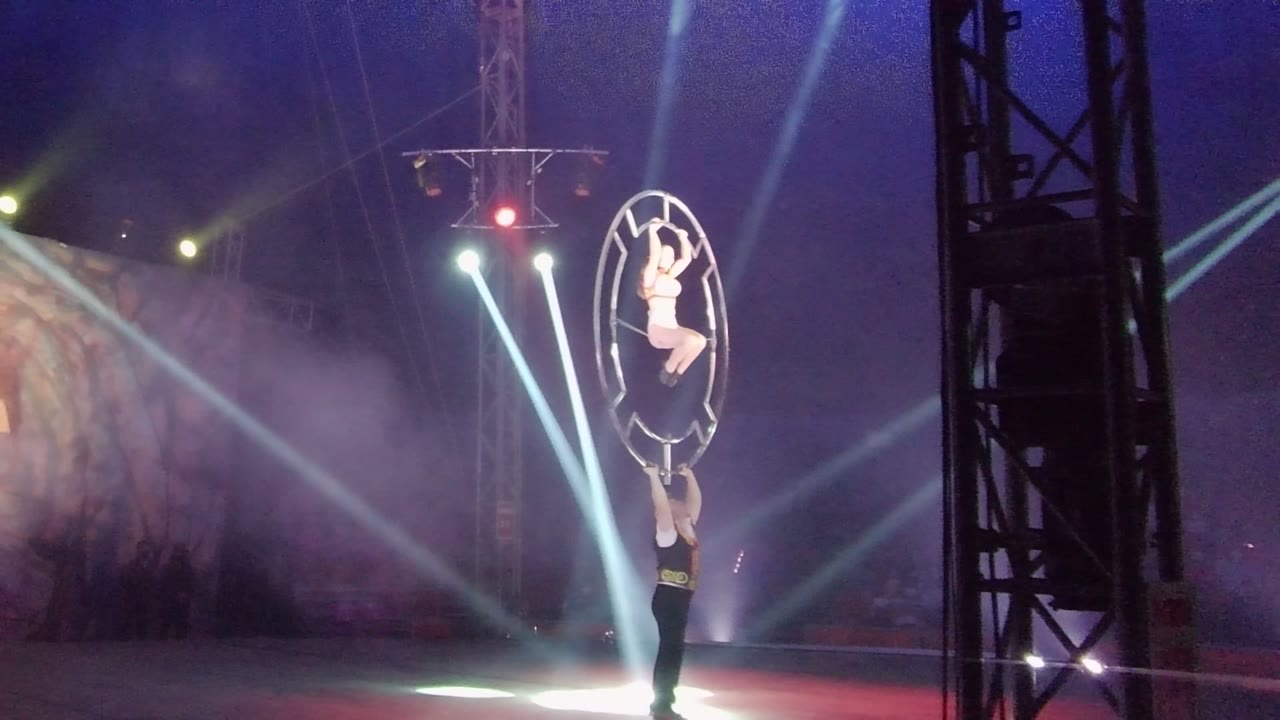 Elevated acrobat sits inside a circular frame above another performer.
