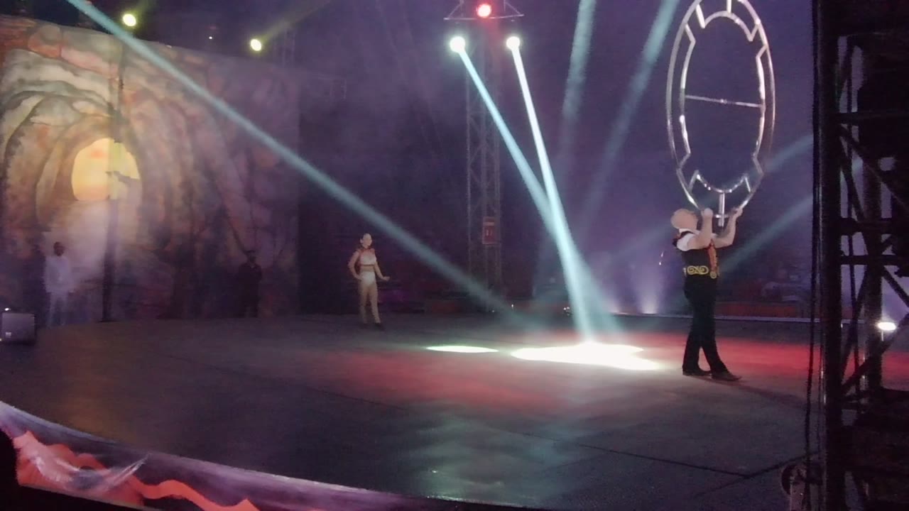 A San Jose Del Cabo BCS Mexico stage frame shows the hoop performer upright near the right edge, the circular prop high beside the body, and a background person lit by haze and spotlights.