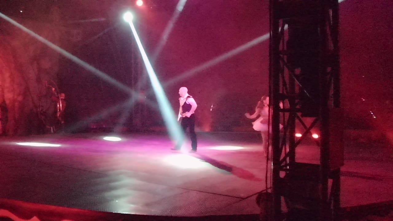 In San Jose del Cabo BCS Mexico, two visible dancers perform on a dark stage as white spotlights cross through red haze and a black truss divides the view.