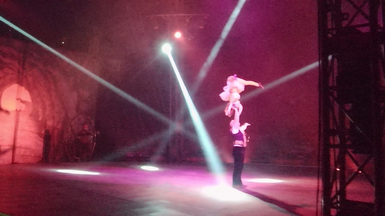 In San Jose del Cabo BCS Mexico, one performer holds another high overhead on a smoky stage with purple-red wash light and bright diagonal spotlights.