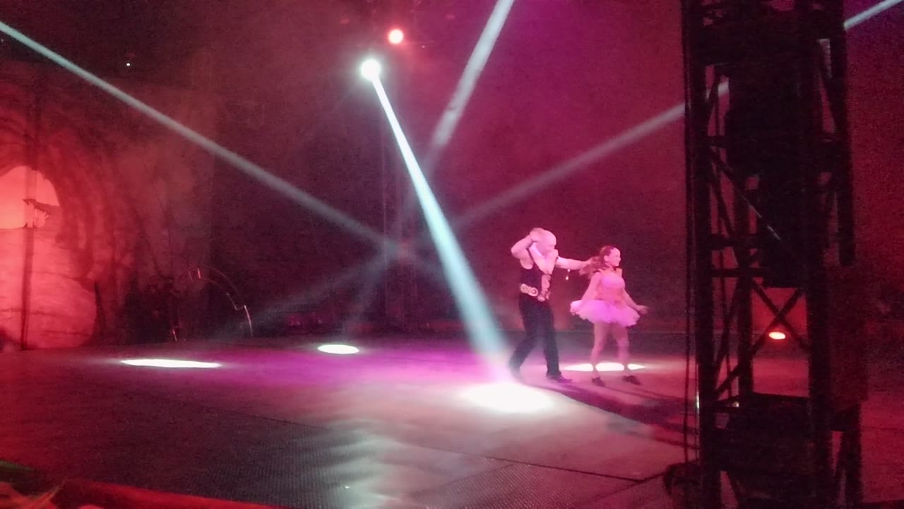 Two dancers perform on a lit stage in San Jose Del Cabo BCS Mexico, with white spotlights crossing above them and a dark truss at the right edge.