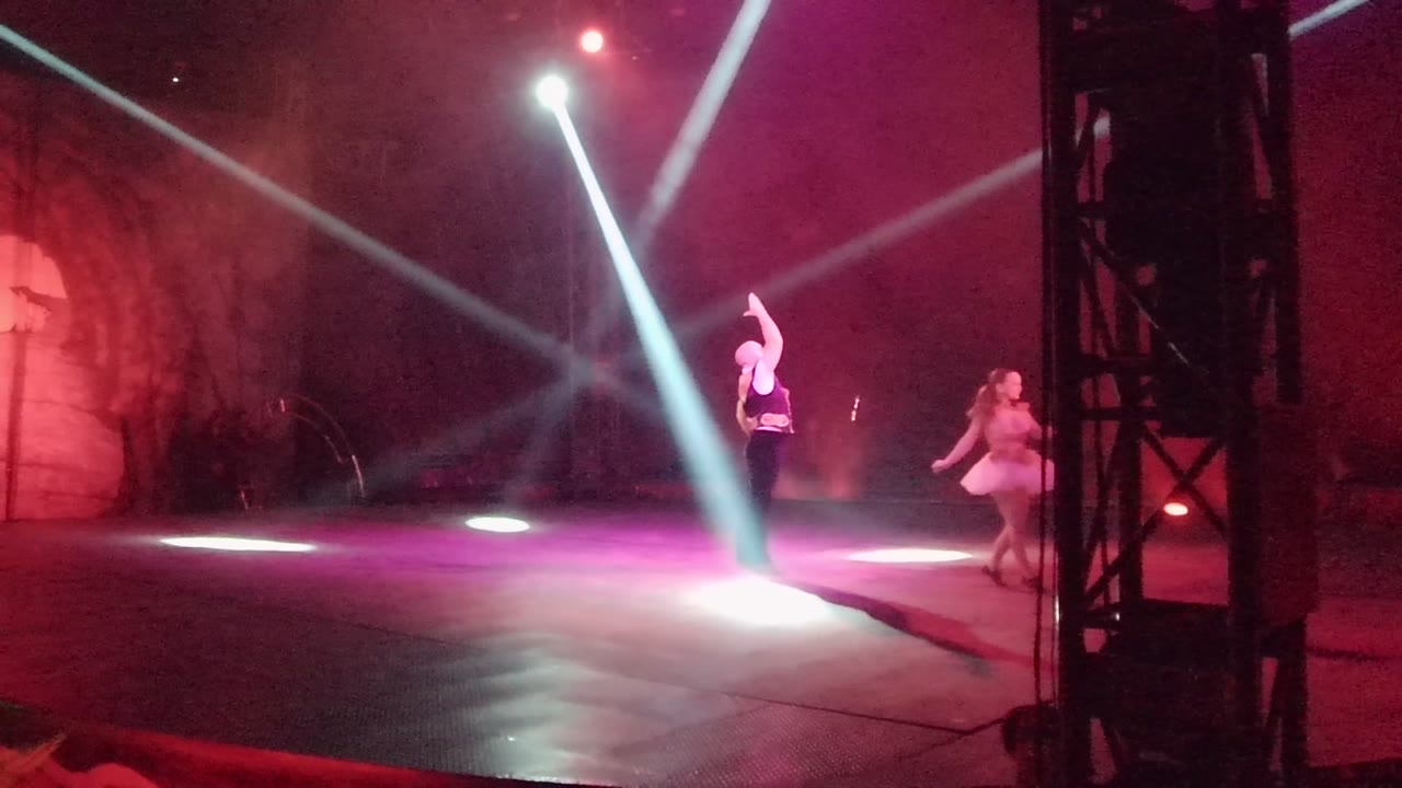 One dancer holds an arm overhead as the second dancer stands to the right on the San Jose Del Cabo BCS Mexico stage under magenta and white lights.