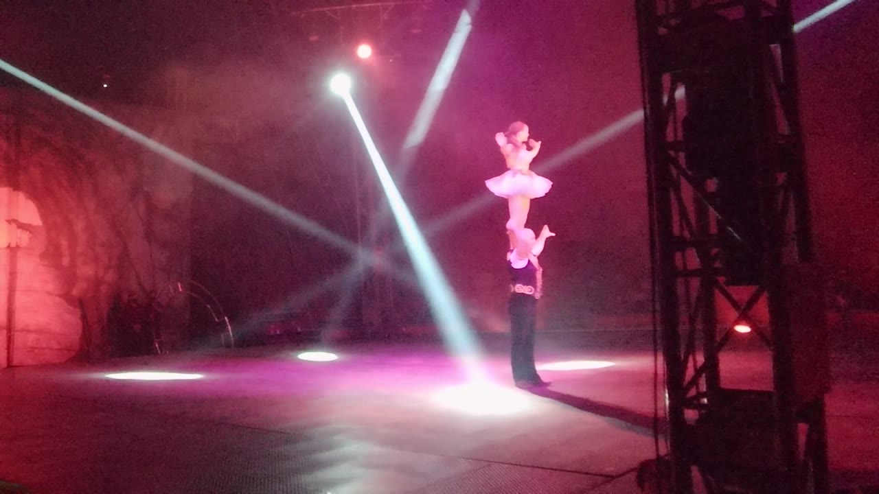 Top performer balances upright above a base performer as white beams cross the stage.