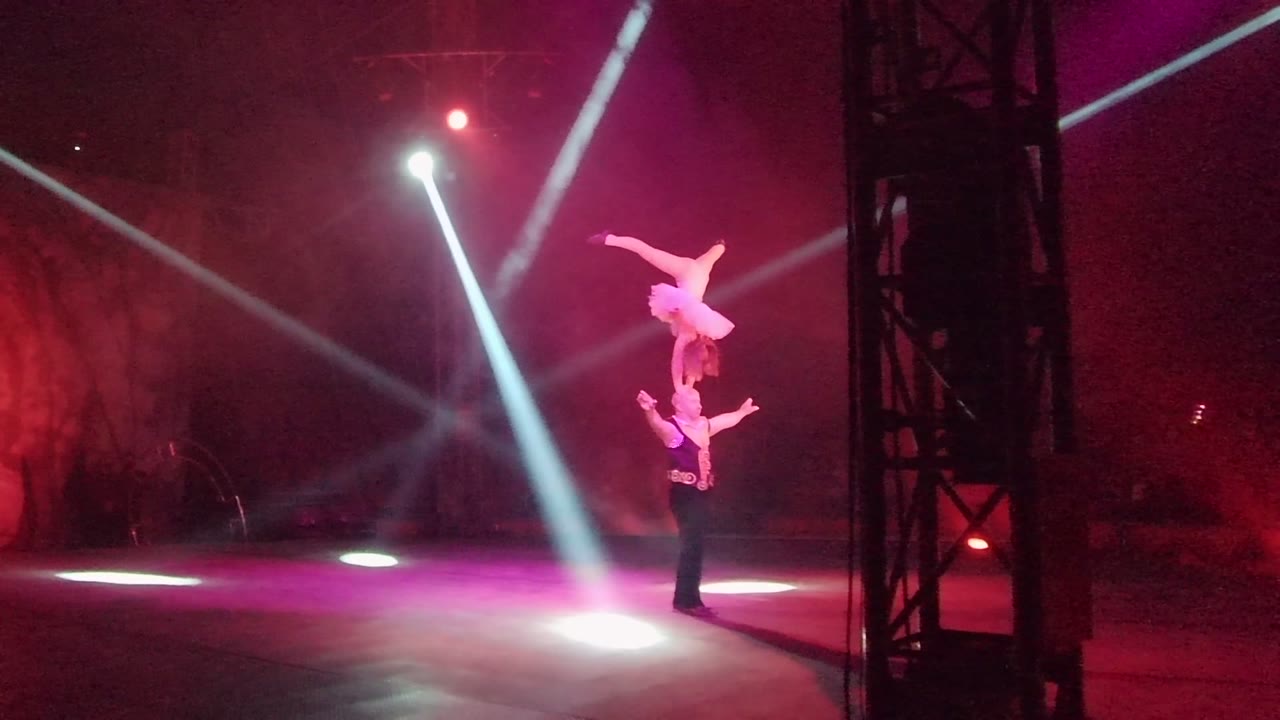 Acrobat held overhead beside crossing spotlights