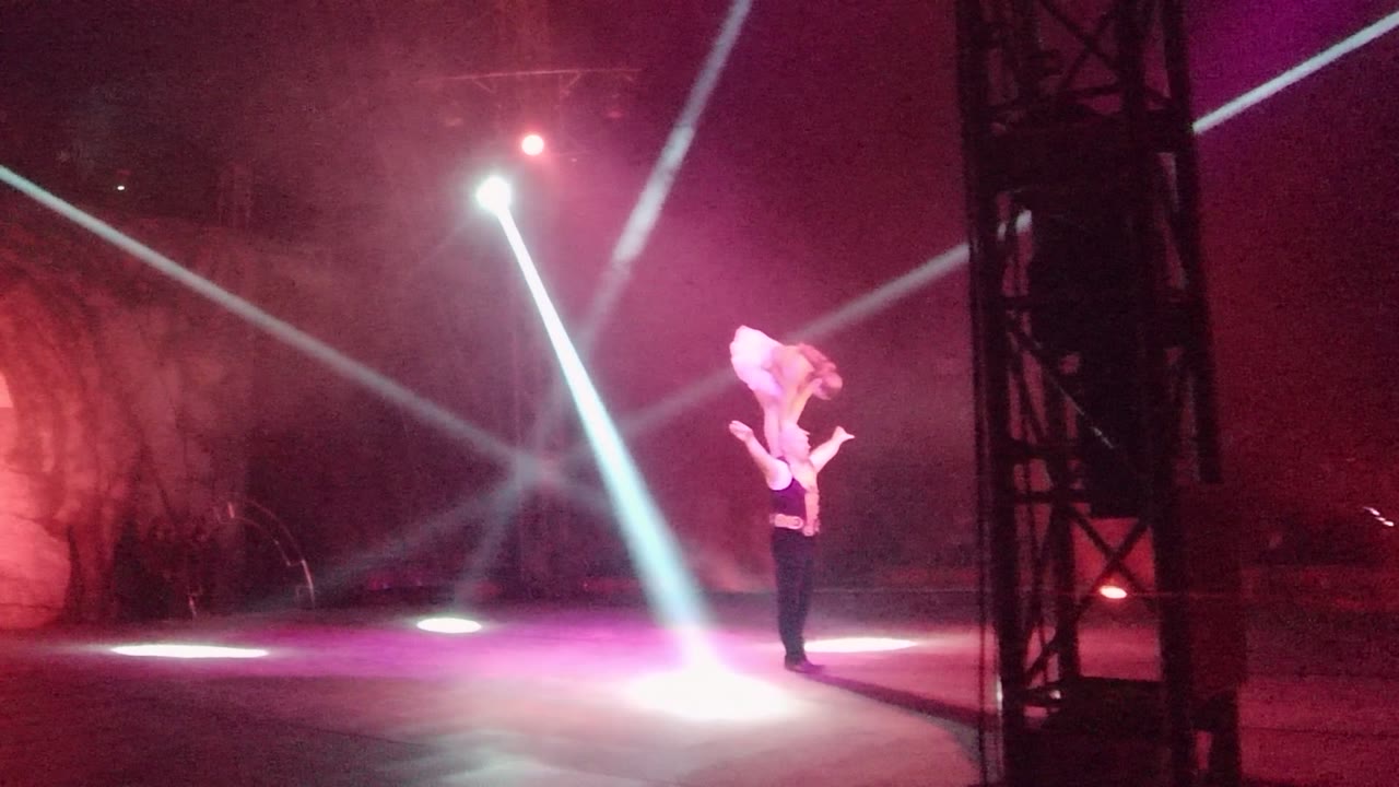 Acrobatic pair shifting position beside a dark stage truss