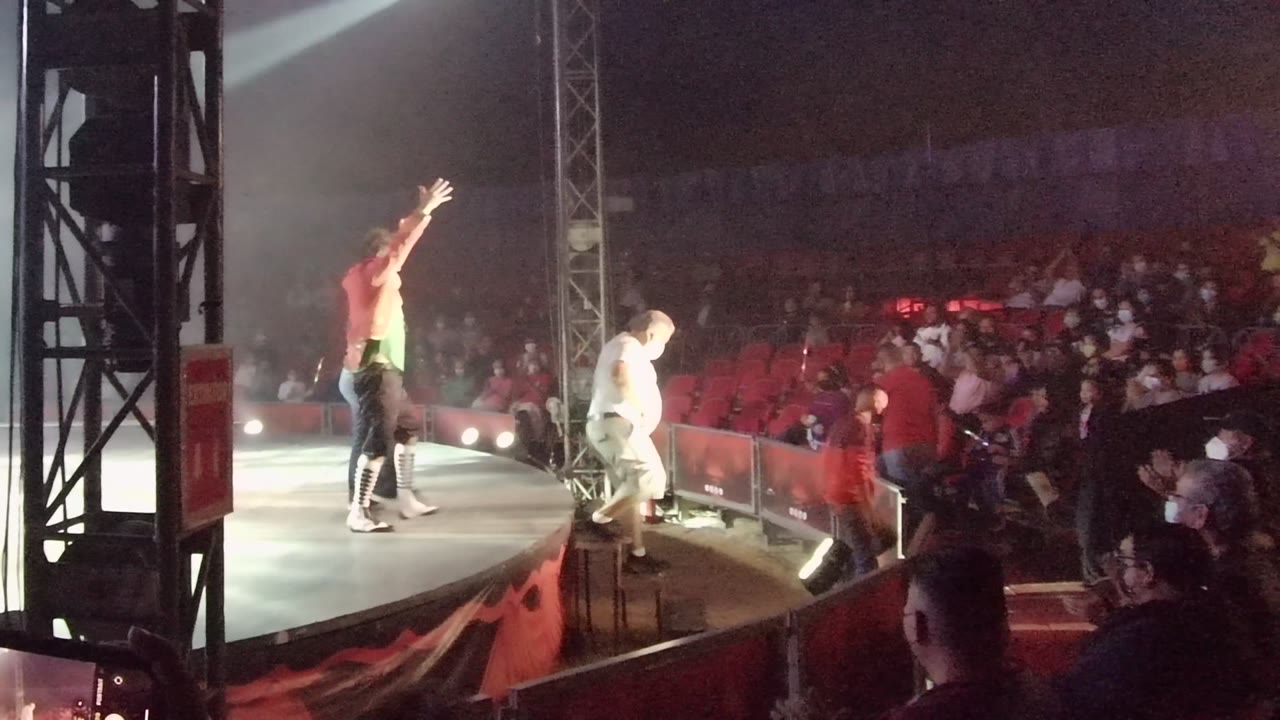 In San Jose del Cabo, Mexico, a red-shirted stage performer raises one arm near the stage edge while audience members watch from behind a barrier.