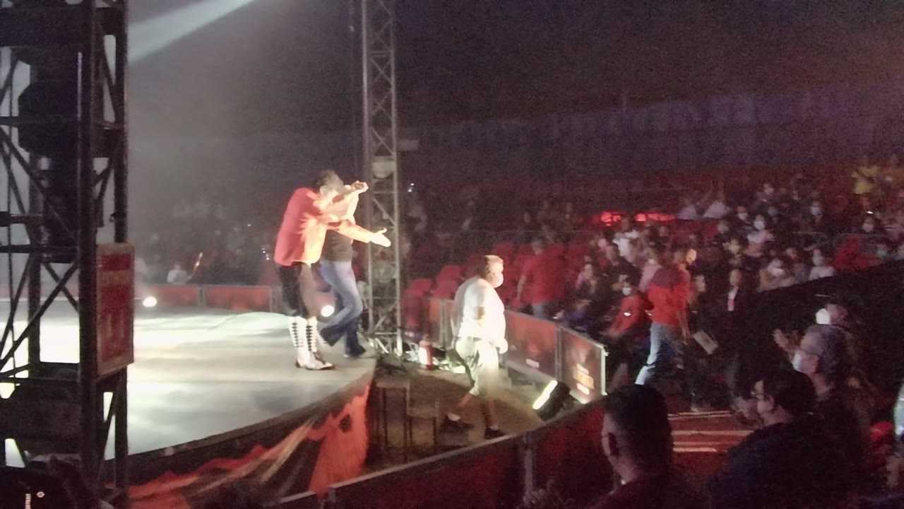 Two performers lean toward the audience from the stage edge.
