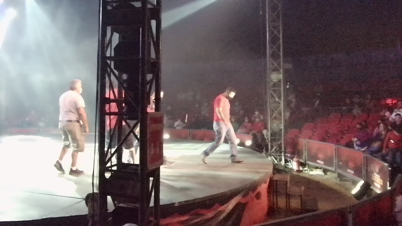 Two adults moving across the stage with red audience seats in the background.