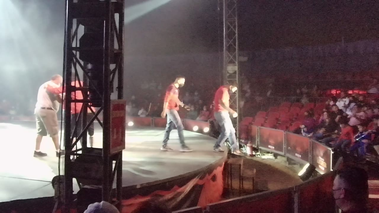 At 0:02 in San Jose del Cabo BCS Mexico, an adult in a red shirt walks near the front of the stage while the audience watches from red seats beyond the barrier.