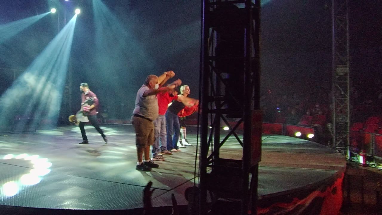 At 0:00 in San Jose del Cabo BCS Mexico, several adults stand on stage as bright spotlights cut through haze and an audience sits beyond the stage edge.
