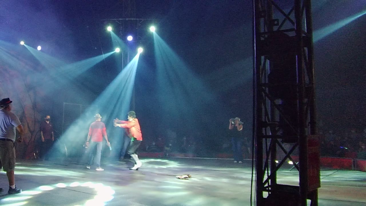 In San Jose del Cabo BCS Mexico, two people in red and orange tops face each other on a stage while spotlights beam through haze and other people stand nearby.