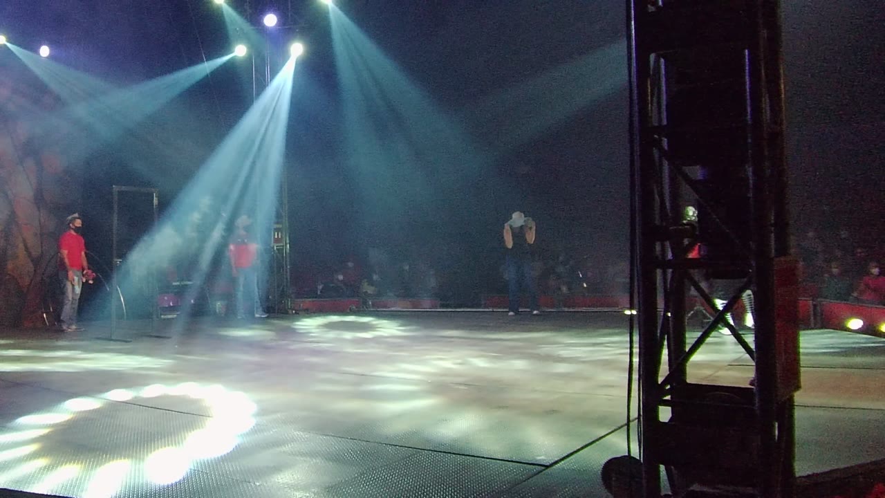 Stage dancers under crossing spotlights with audience in the background.