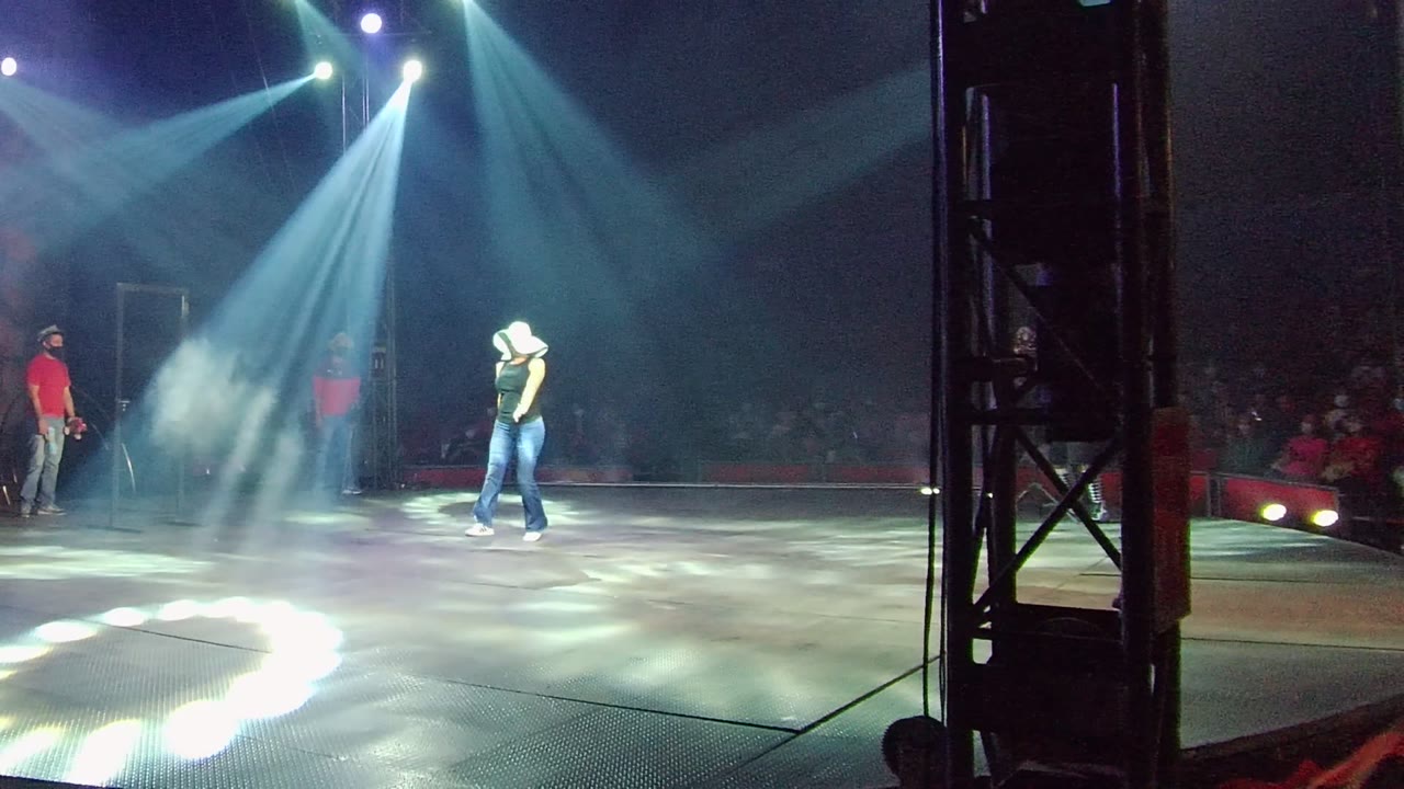 In San Jose Del Cabo BCS Mexico, a cowboy-hat performer walks across a stage under blue-white spotlights while audience members sit in the dark background.