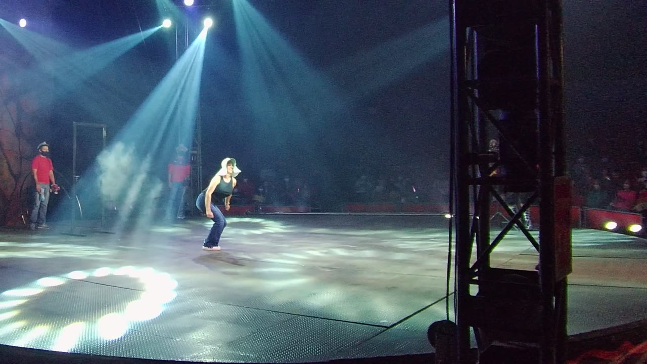 In San Jose Del Cabo BCS Mexico, the performer bends forward near center stage while a crew member in red stands near the darker audience area.