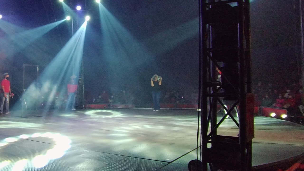 Wide stage view with spotlights, haze, red-shirted person, and performer in jeans.
