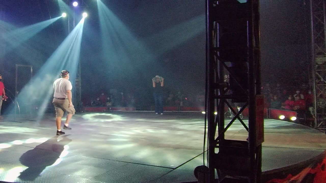 The performer reaches the center of the illuminated stage in San Jose del Cabo, Mexico, with a long shadow stretching across the floor and audience members dimly visible behind.